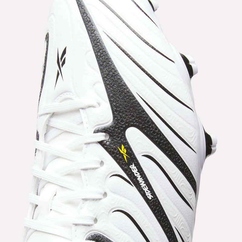 Close-up of the Reebok Sidewinder 26 League Firm Ground Cleats in white, featuring black textured patterns, black and yellow Reebok logos, and white laces. Designed for excellent ball control, these cleats are equipped with firm ground studs that offer optimal traction on natural grass surfaces—making them ideal for precision play.