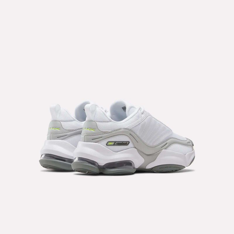 A pair of Reebok Women’s DMX Series 3000 Shoes, featuring white and gray uppers with chunky soles and neon green accents, is shown from a rear angle against a plain light background. These ultra-cushioned sneakers provide lightweight support designed for all-day comfort.