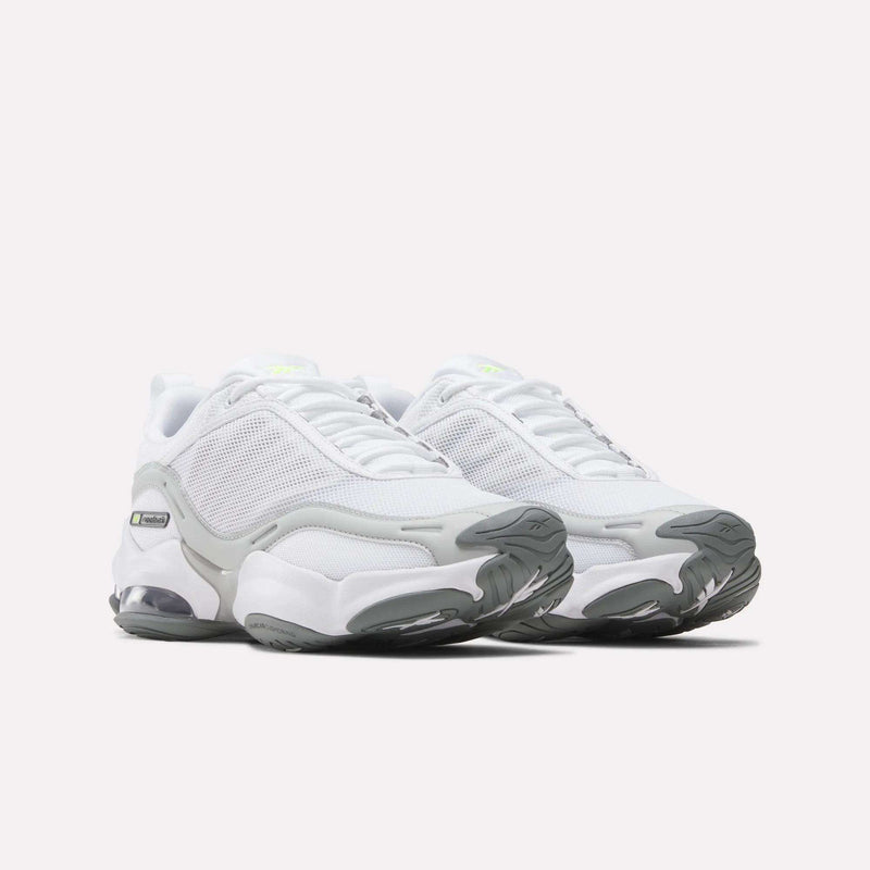 The Reebok Women’s DMX Series 3000 Shoes are a pair of white athletic sneakers with gray accents and chunky soles, positioned side by side on a plain light background, offering lightweight support and ultra-cushioned comfort with innovative DMX moving air technology.
