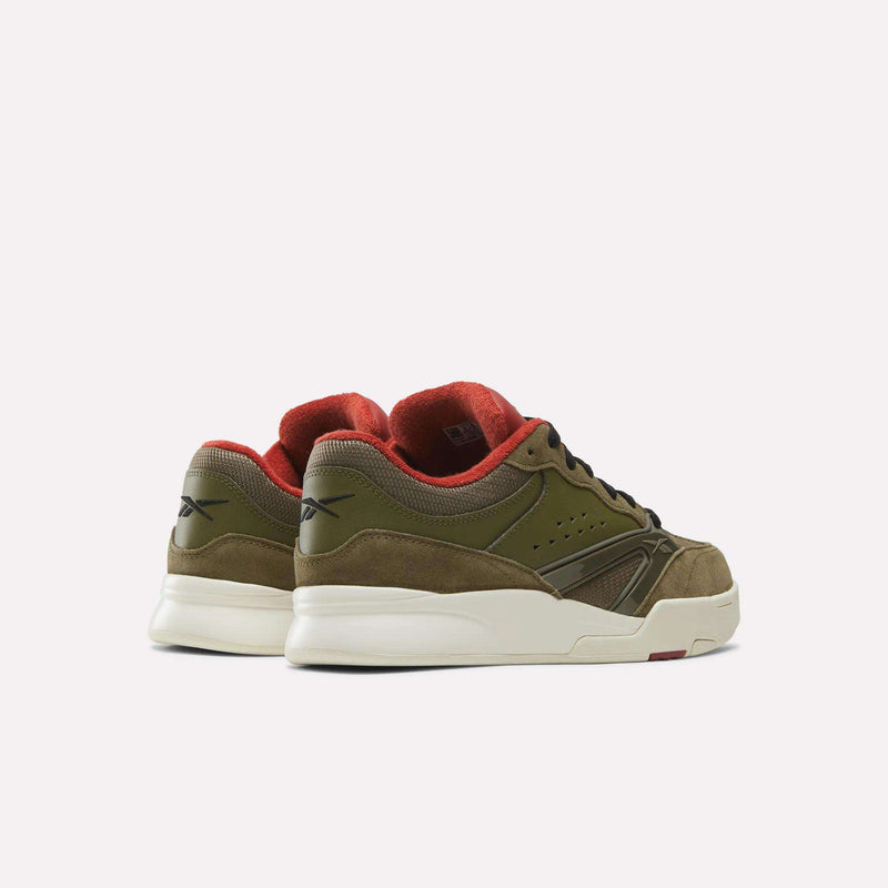 A pair of Reebok Omni Edge Shoes in olive green and beige is displayed from the back on a plain white background, showcasing their classic silhouette inspired by iconic basketball court styles. The bold red inner lining adds a striking contrast to these premium sneakers.