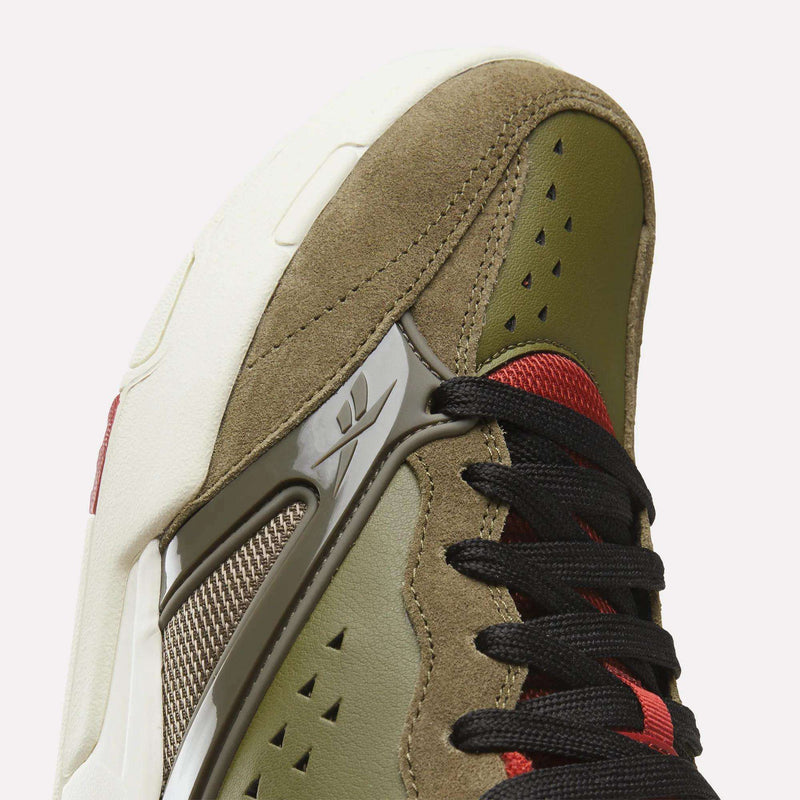 Close-up of the Reebok Omni Edge Shoes, a premium sneaker designed with olive green and tan suede panels, black laces, red mesh accents, perforations, Reebok’s signature side logo, and an off-white rubber sole inspired by classic basketball court styles.