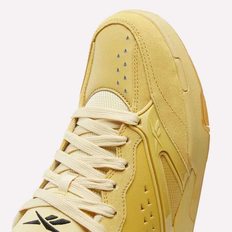 Close-up of a pale yellow Reebok Omni Edge sneaker with a suede-like texture, featuring mesh panels, flat laces, and perforated detailing on the toe box.