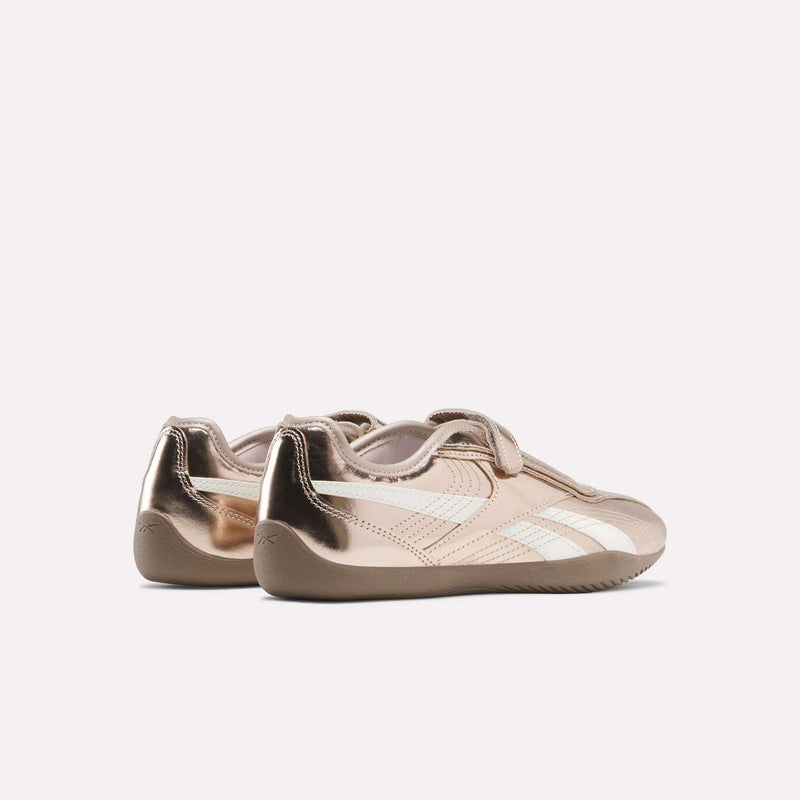 A pair of Women’s Ultra Lo Mary Jane Shoes by Reebok in metallic rose gold leather, featuring white stripes and tan soles, are positioned side by side on a plain light background, facing slightly away.