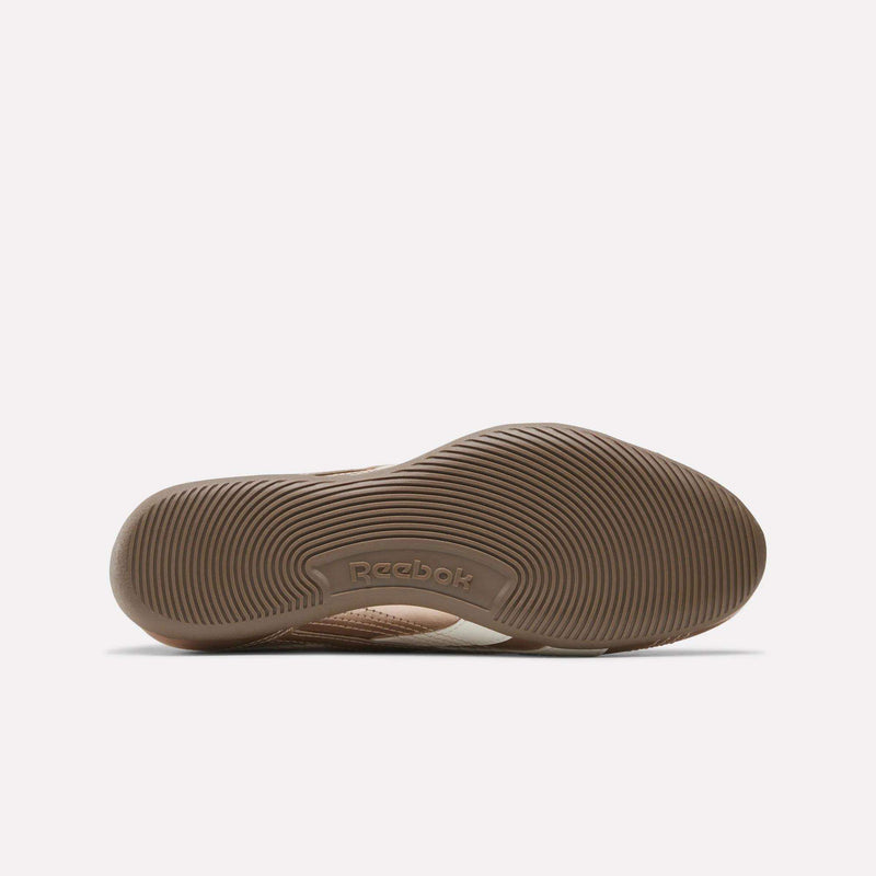 The image displays the brown, textured sole of a Women’s Ultra Lo Mary Jane Shoe by Reebok, as seen from the bottom. The sole is designed with circular patterns, and the Reebok logo appears in the center.