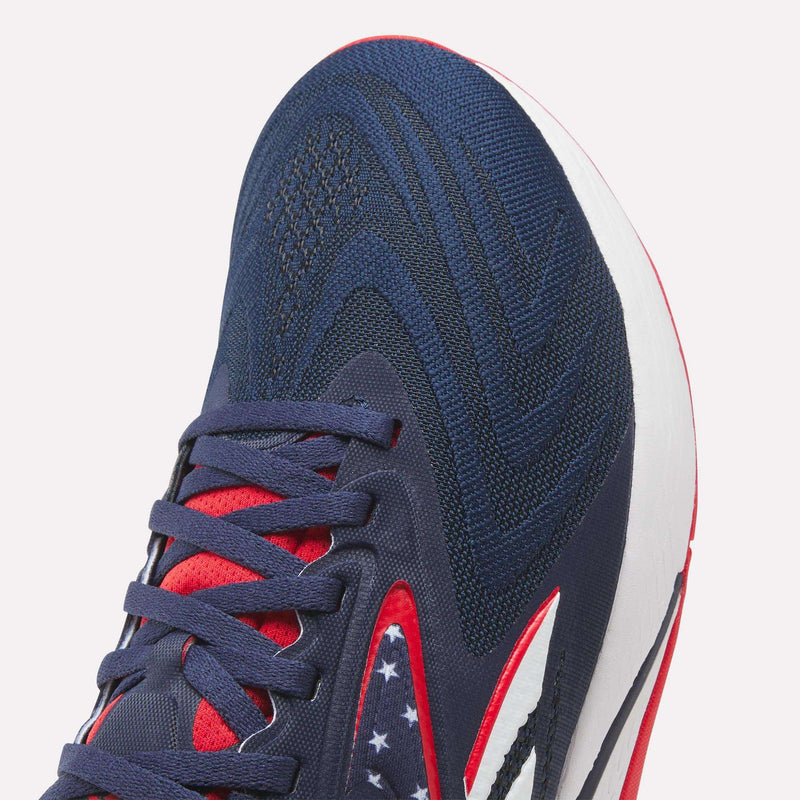 Close-up of Reebok Nano X5 Edge Training Shoes in navy with red and white accents, patterned laces, and white stars on a dark blue section. Featuring a Flexweave upper and white midsole for durability—ideal for precision training.