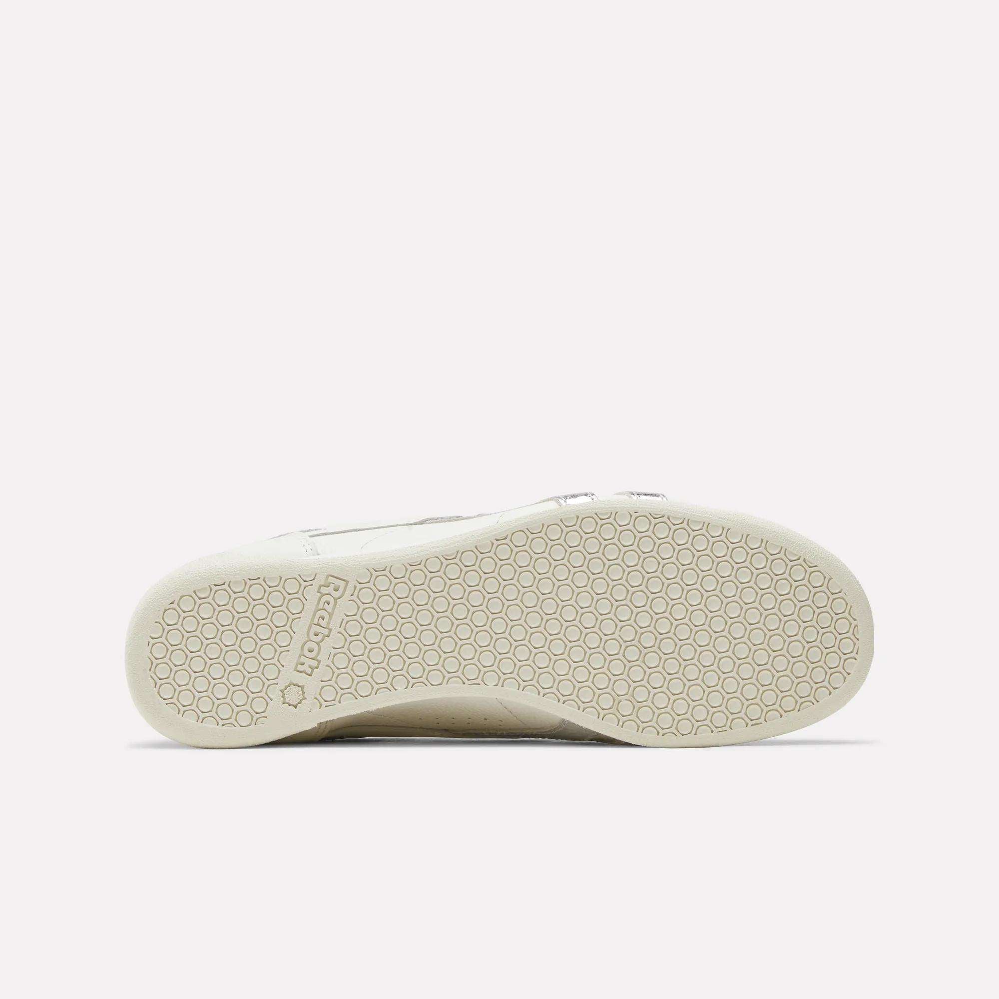 The image displays the bottom view of Reebok Women's Freestyle Lo Shoes, showing a textured sole with a hexagonal pattern and the Reebok logo near the heel.