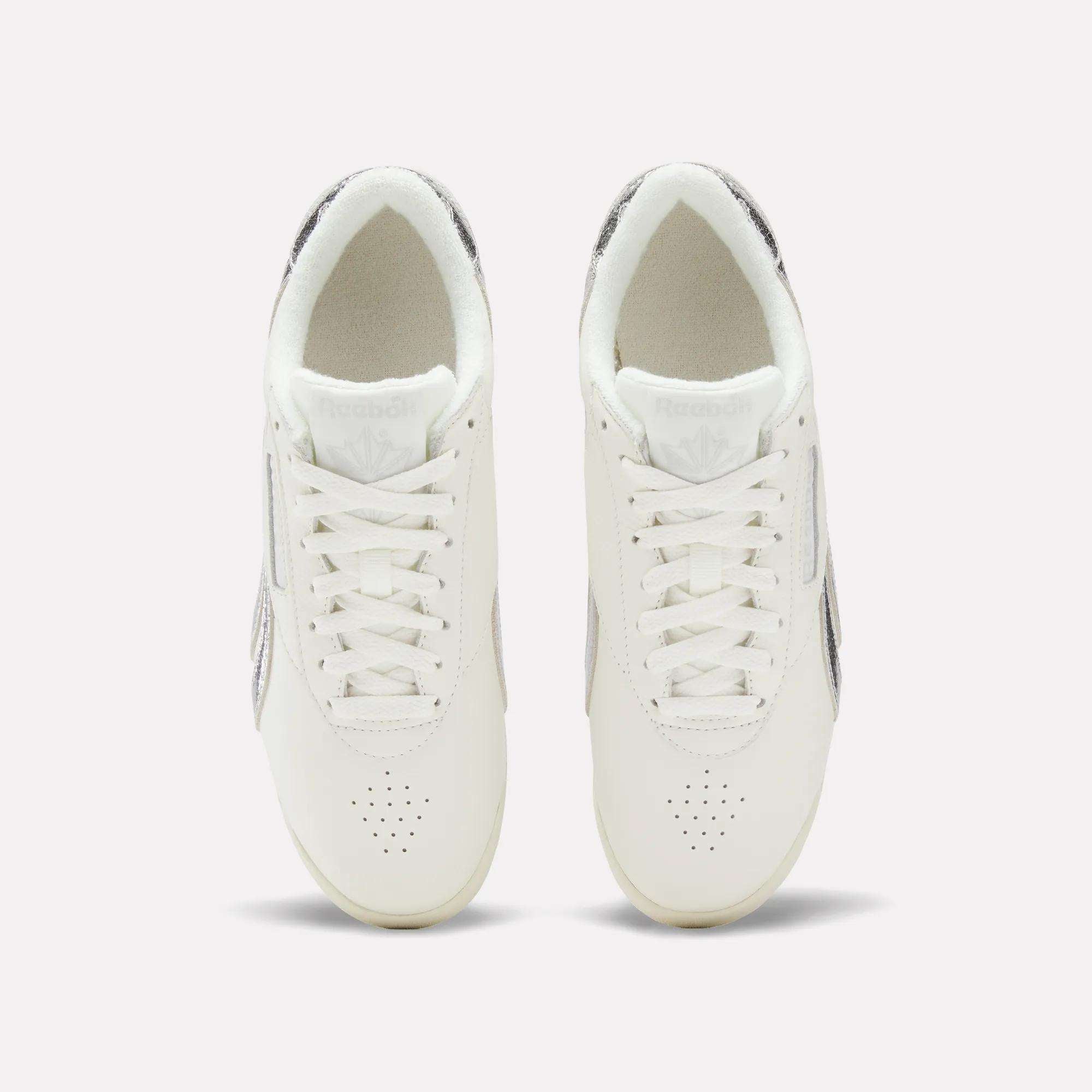 Top view of Reebok Women's Freestyle Lo Shoes with laces and subtle metallic accents on the sides and heel, displayed against a simple light background.