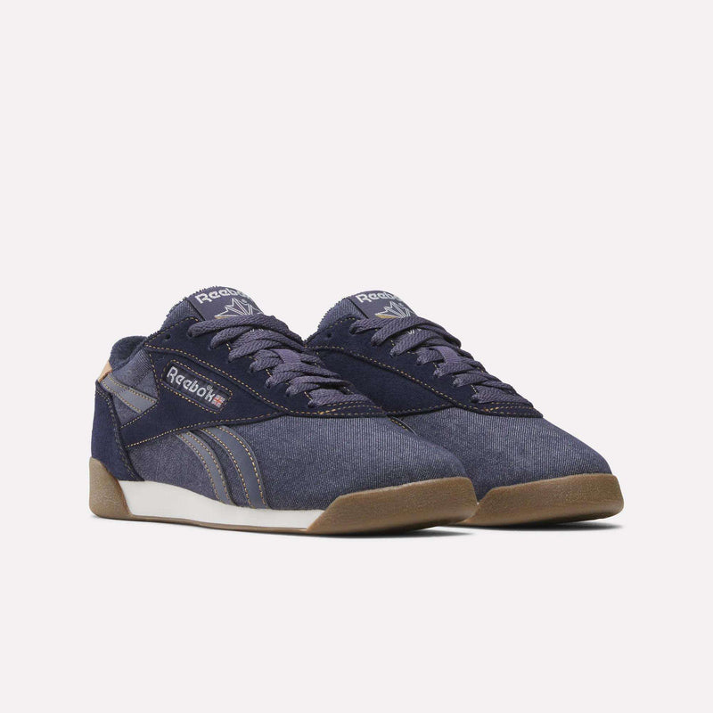 A pair of Women’s Freestyle Lo Shoes by Reebok, featuring navy blue uppers with dark blue laces, white midsoles, and gum soles, displayed at an angle against a plain white background—timeless women’s sneakers with subtle vintage denim-inspired appeal.