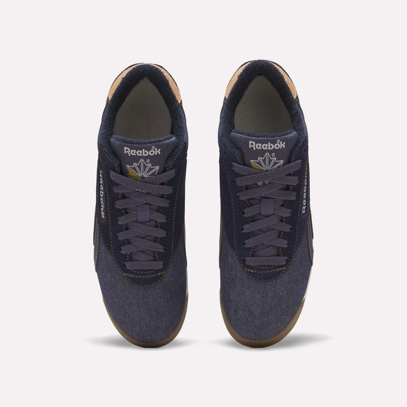 A top view of a pair of Women’s Freestyle Lo Shoes by Reebok in navy blue with purple laces, tan inner lining, and gum soles, arranged side by side on a plain white background—these vintage-inspired sneakers are a timeless addition to women’s footwear collections.