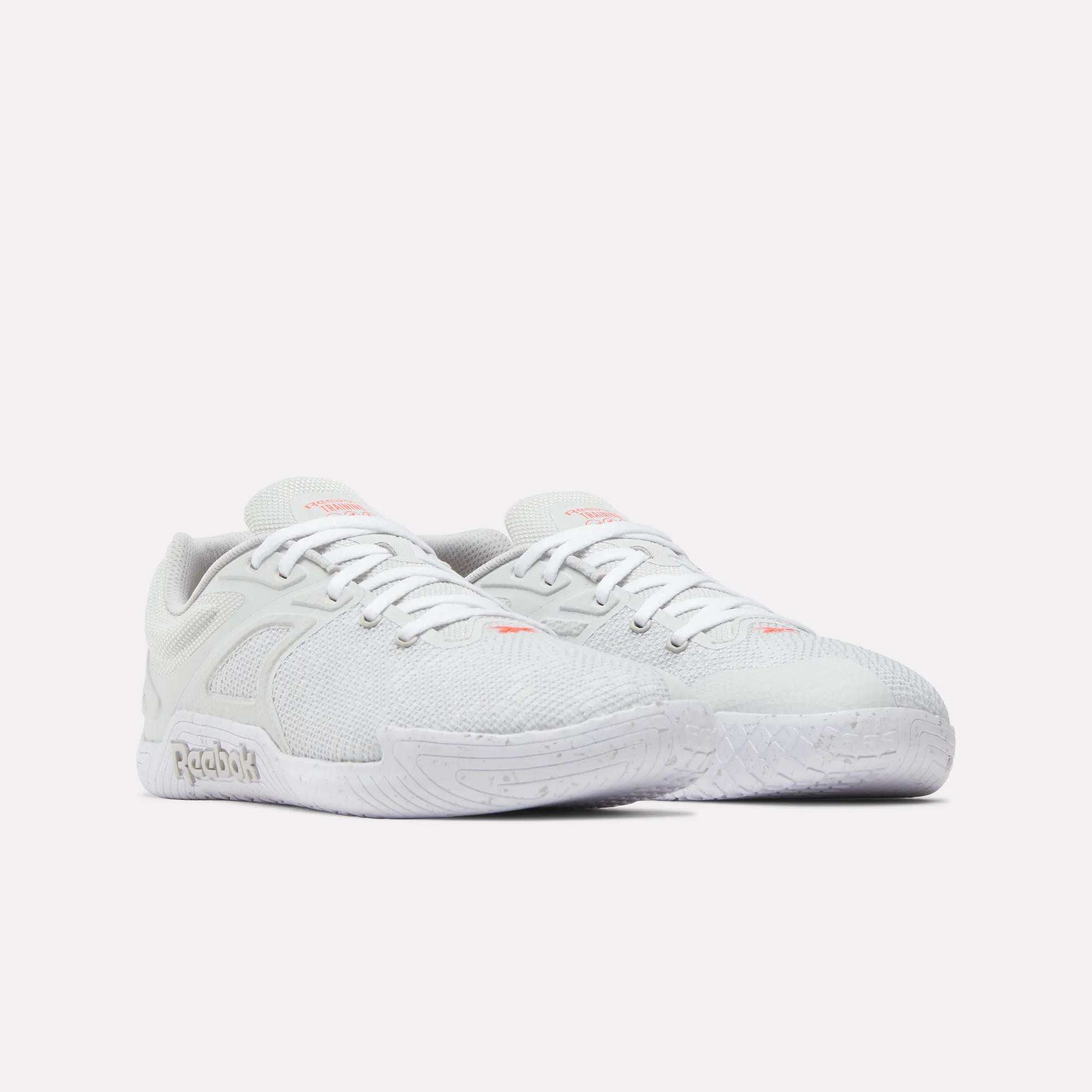 A pair of Reebok Nano Zero Training Shoes in white with subtle pink accents, textured mesh uppers, laces, and cushioned soles is displayed against a plain white background.