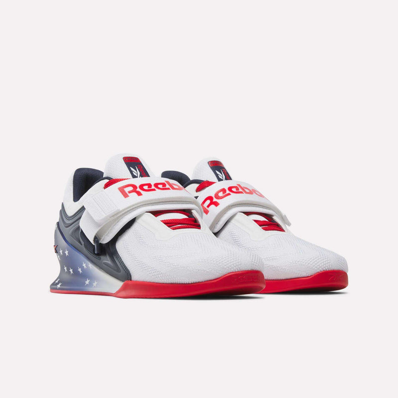 Reebok Men's Legacy Lifter IV Shoes: white lifting shoes with red soles, red and navy accents, a white top strap, plus a navy heel section with white stars for added workout stability.