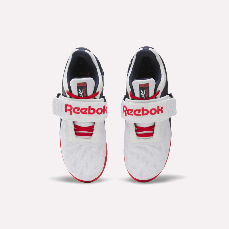 A pair of Reebok Men's Legacy Lifter IV Shoes in white with red accents, featuring thick white straps across the top labeled "Reebok" in bold red letters, viewed from above against a plain background for added stability.