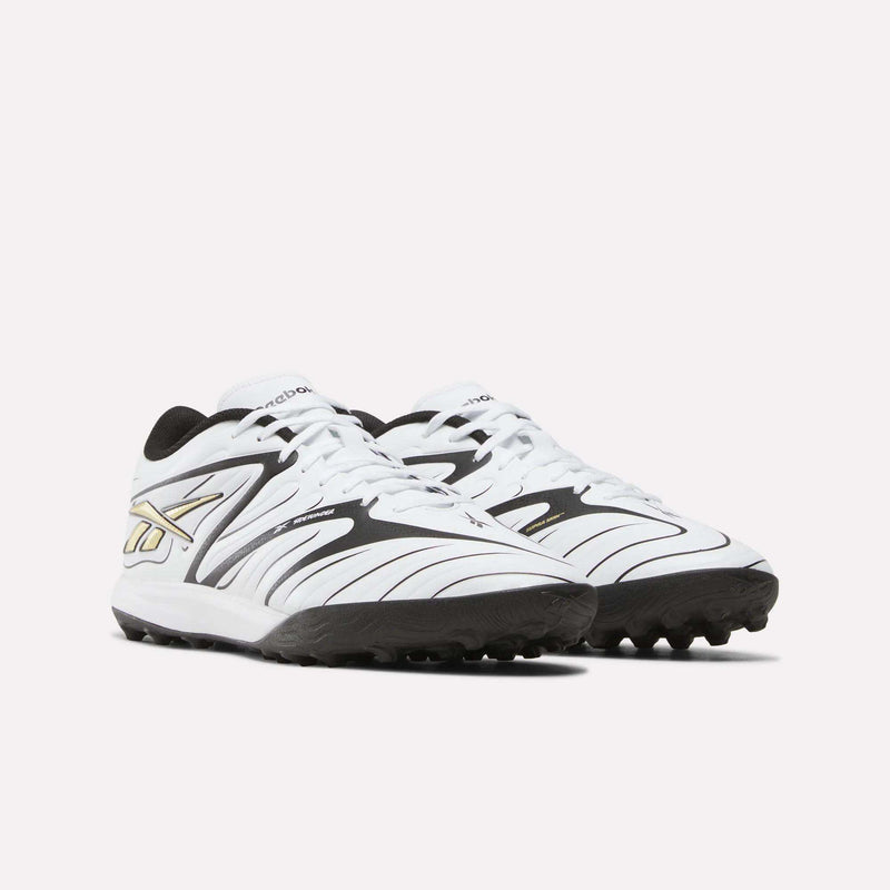 A pair of Reebok Sidewinder 26 League Turf Cleats in white and black with gold accents, designed for turf players, displayed side by side on a plain white background.