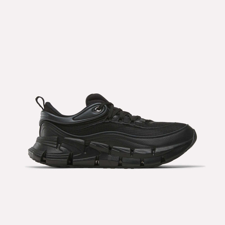 The Reebok Floatzig Encore Running Shoes in Black/Black are athletic sneakers inspired by Reebok’s running heritage, featuring a chunky sole, mesh upper, lace-up front, and a pull tab at the heel. Designed for walking and fitness, they are displayed against a plain white background.