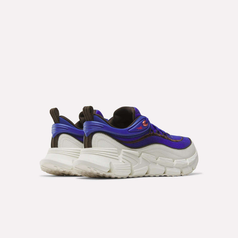 A pair of Reebok Floatzig Encore Running Shoes featuring chunky white thick soles, purple uppers with black and brown accents, and convenient pull tabs at the heel, displayed against a plain light background. Ideal for walking and fitness, these shoes offer bold Zig tech style combined with superior comfort.