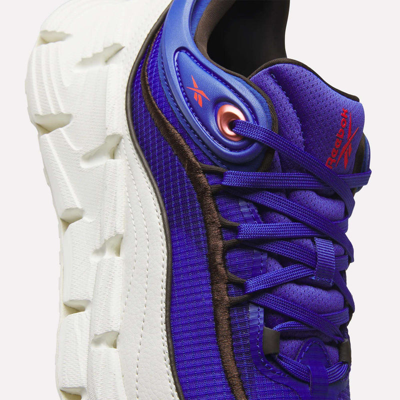 Close-up of a purple and blue Reebok Floatzig Encore Running Shoe featuring a thick, textured white sole and red logo accents—designed for walking and fitness, this shoe combines style with innovative performance.