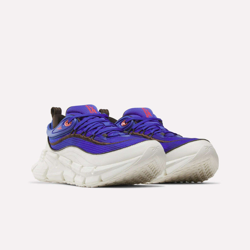 A pair of chunky Floatzig Encore Running Shoes by Reebok, in blue and purple with thick white soles, red accents, textured grip, and signature Zig tech shoes technology for walking and fitness—displayed against a plain white background.