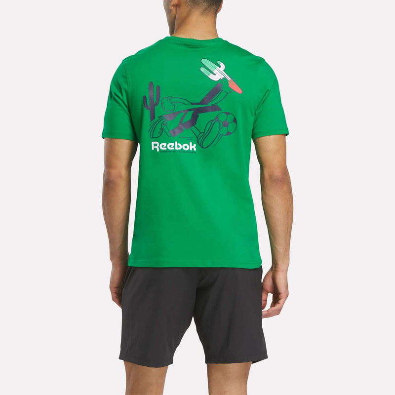 A man is seen from the back wearing a green Reebok Mexico Football T-Shirt with sports-themed graphics and black shorts. This cotton crewneck features a cactus, basketball, soccer ball, and airplane in its vibrant design.