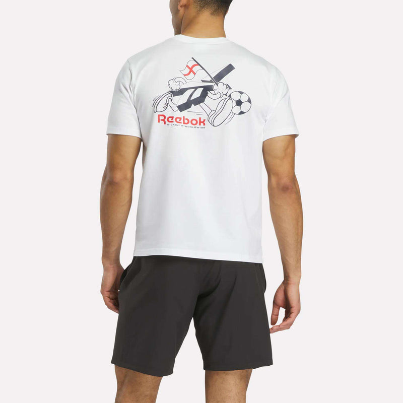A man stands with his back to the camera, wearing a white Reebok England Football T-Shirt featuring a cartoon graphic and text on the back, paired with black shorts, against a plain background.