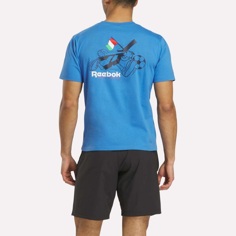 A man faces away wearing a blue Italia Football T-Shirt by Reebok, crafted from soft cotton jersey with sports-themed graphics and Italian flag colors. He completes his sporty look with black shorts.