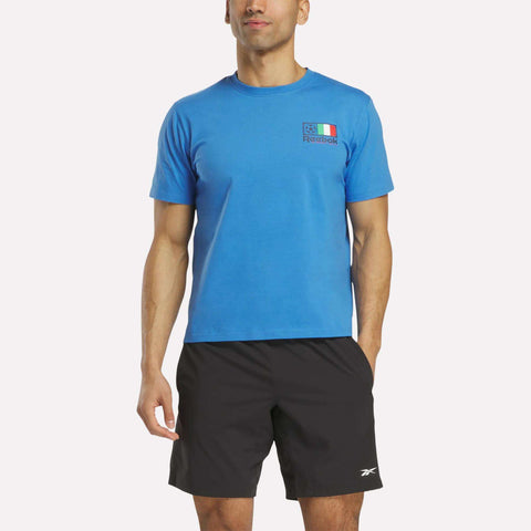 A man wearing a blue Reebok Italia Football T-Shirt with a small logo and black Reebok shorts stands against a plain white background.