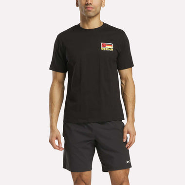 A man wears a black Reebok Deutschland Football T-Shirt with a small chest logo and black Reebok shorts, standing against a plain white background.