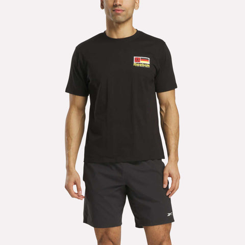 A man wears a black Reebok Deutschland Football T-Shirt with a small chest logo and black Reebok shorts, standing against a plain white background.