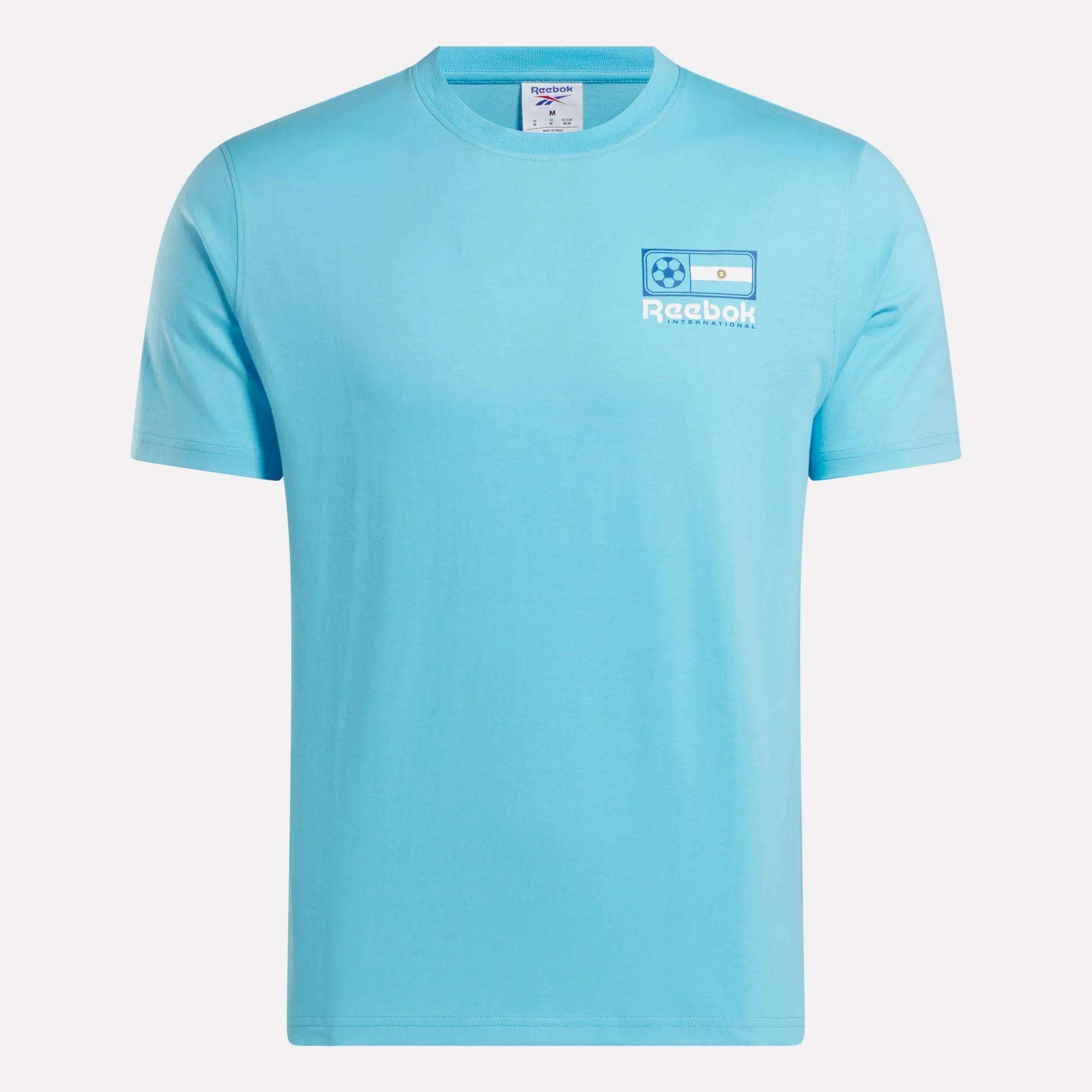 The Reebok Argentina Football T-Shirt is a light blue cotton tee with a small left chest logo featuring the Argentina flag, soccer ball, and "Reebok" in white—a great choice for Argentina fans.