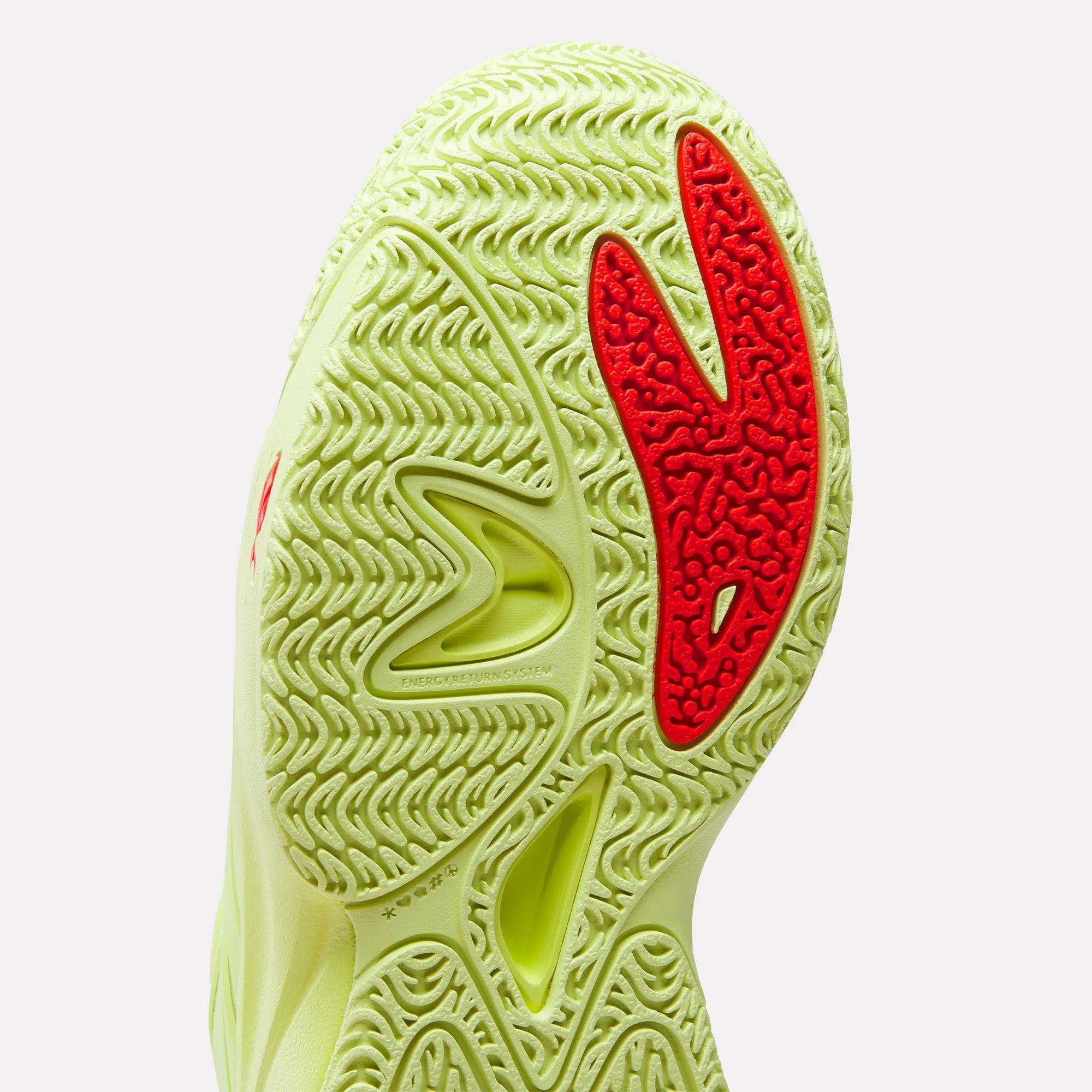 Close-up of the Reebok Angel Reese 1 Shoes – Big Kids, featuring a wavy, textured yellow-green sole with bold red accents and detailed grooves for traction—showcasing signature performance basketball shoe design.