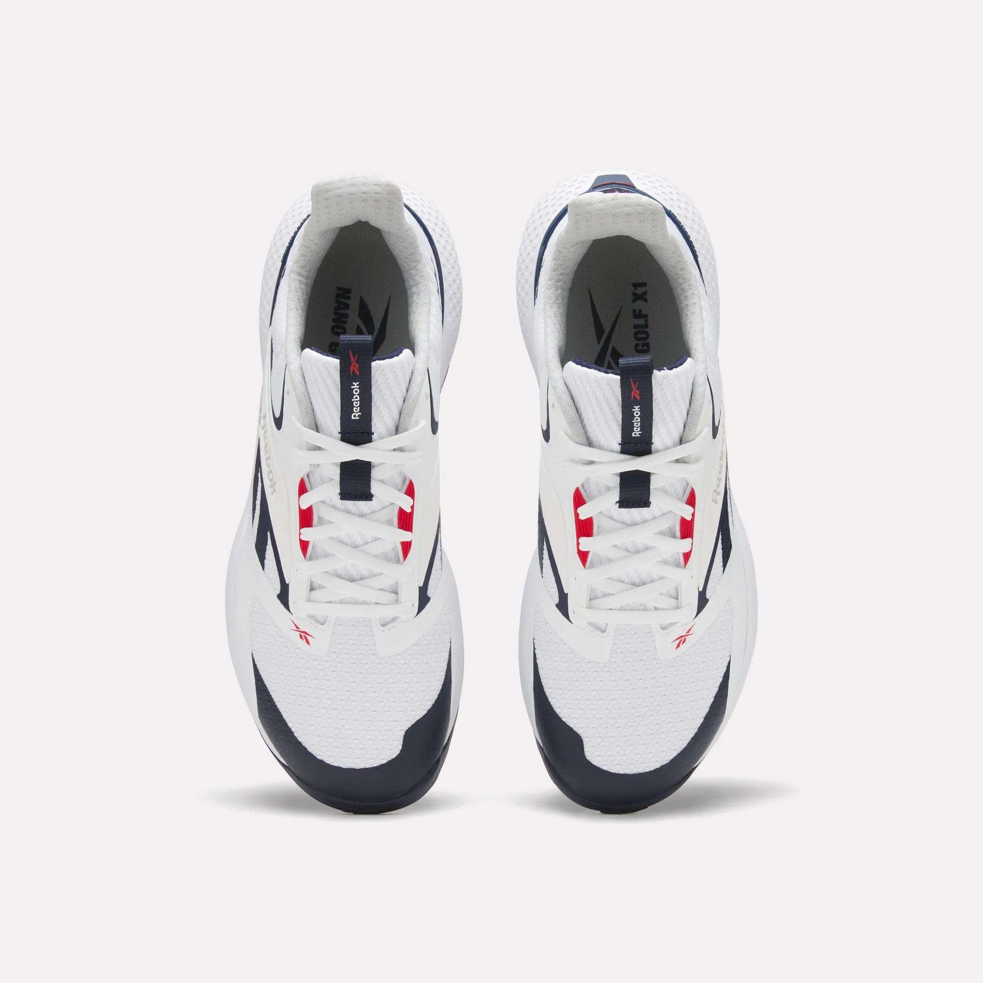 Top view of a pair of white Reebok Nano Golf Shoes with navy and red accents, white laces, black outsoles, and lightweight FlexWeave for comfort, positioned side by side on a plain light background.