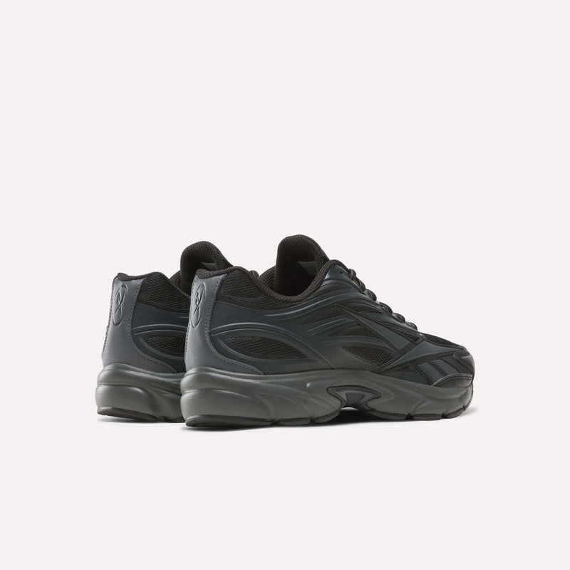 A pair of Reebok Premier Road 1000 Shoes in black, featuring a chunky sole and distinctive wavy side details, are displayed on a white background at an angle that highlights the outer side and back—these retro-inspired Y2K sneakers blend nostalgic style with modern comfort.