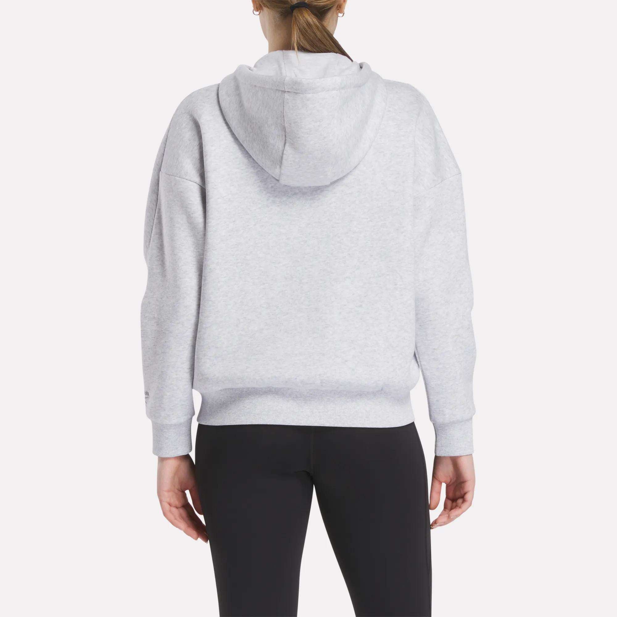 A person faces away from the camera wearing a Women's Reebok x F45 Training Relaxed Zip Hoodie in light gray and black leggings, set against a plain white background.