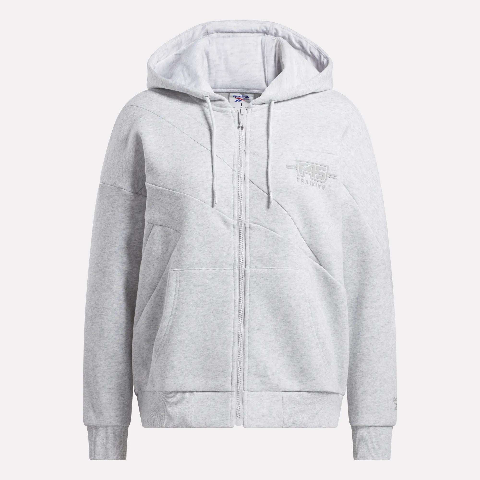 The Women's Reebok x F45 Training Relaxed Zip Hoodie features a hood, front pockets, subtle seams, and a small logo with TRAINING on the chest. This light gray fleece hoodie offers soft comfort for everyday wear and F45 Training.