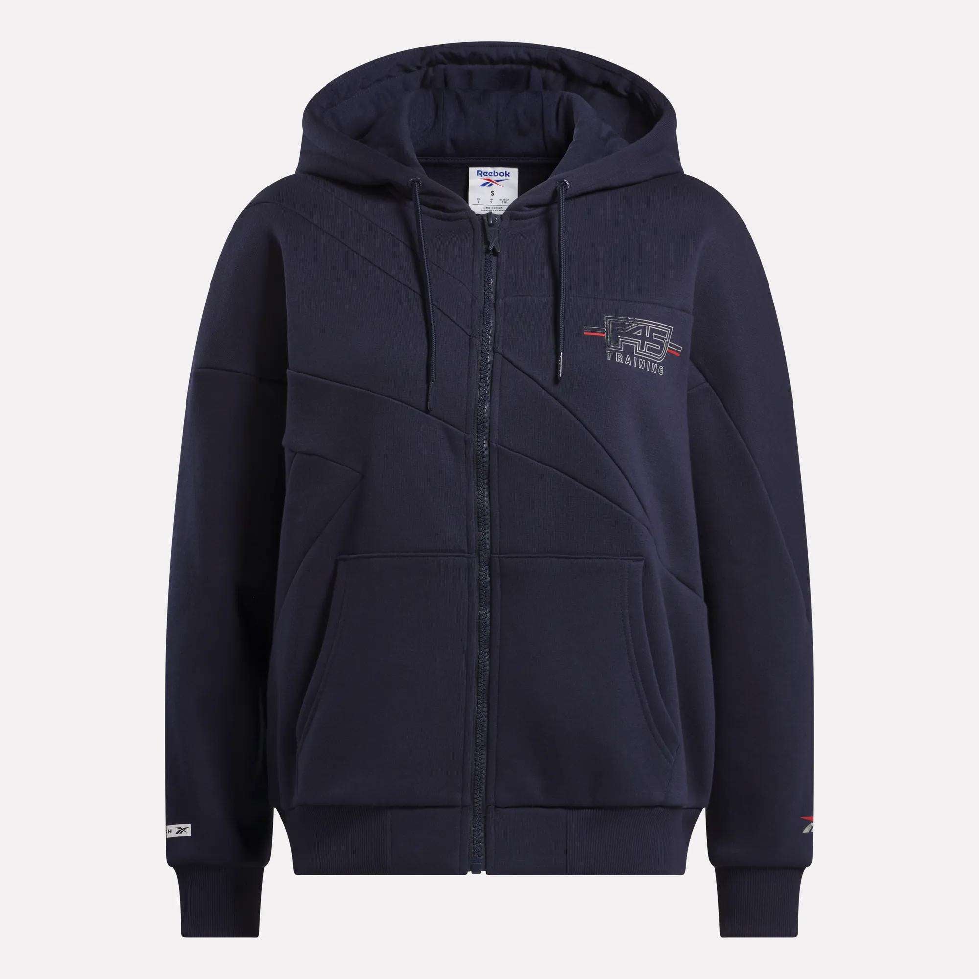 Stay stylish at F45 with the women's Reebok x F45 Training Coach Full-Zip Hoodie in navy blue, featuring a hood, front pockets, geometric stitching, and subtle embroidered logos on the chest and sleeve.