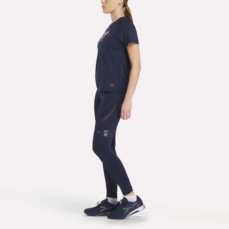 A woman with a ponytail stands sideways against a white background, wearing a matching navy blue Reebok outfit featuring the Reebok x F45 Training Coach Lux Leggings and a t-shirt, paired with sneakers.