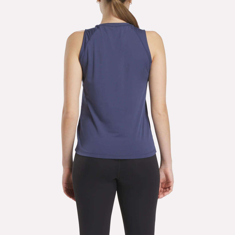 A woman with a ponytail wears the Women's Reebok x F45 Training Tank Top in purple and black leggings, standing with her back to the camera. The Reebok sweat-wicking fabric helps keep her cool during F45 workouts.