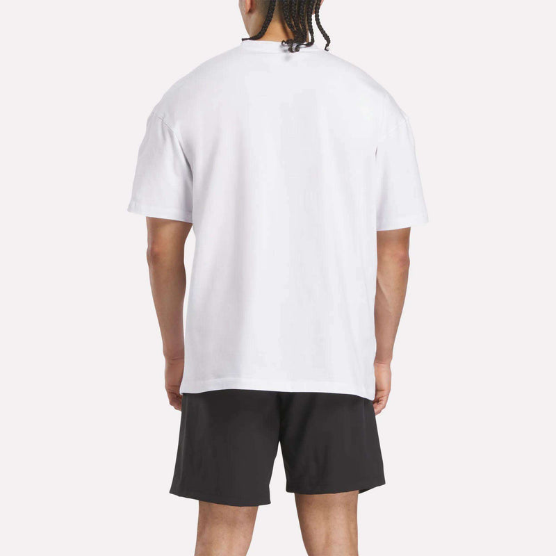 A person is standing and facing away from the camera, wearing a plain white Reebok x F45 Training Relaxed T-Shirt and black shorts against a light background.