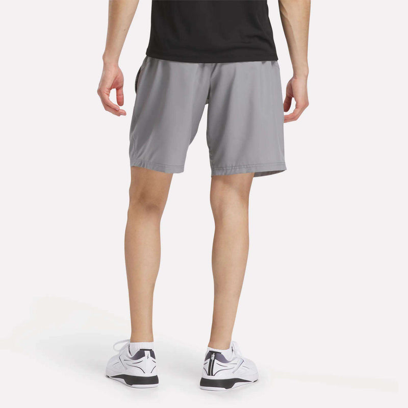 A person in a black shirt, Reebok x F45 Training Woven Shorts, and white sneakers stands with their back to the camera against a plain white background—perfect for high-intensity or F45 workouts.