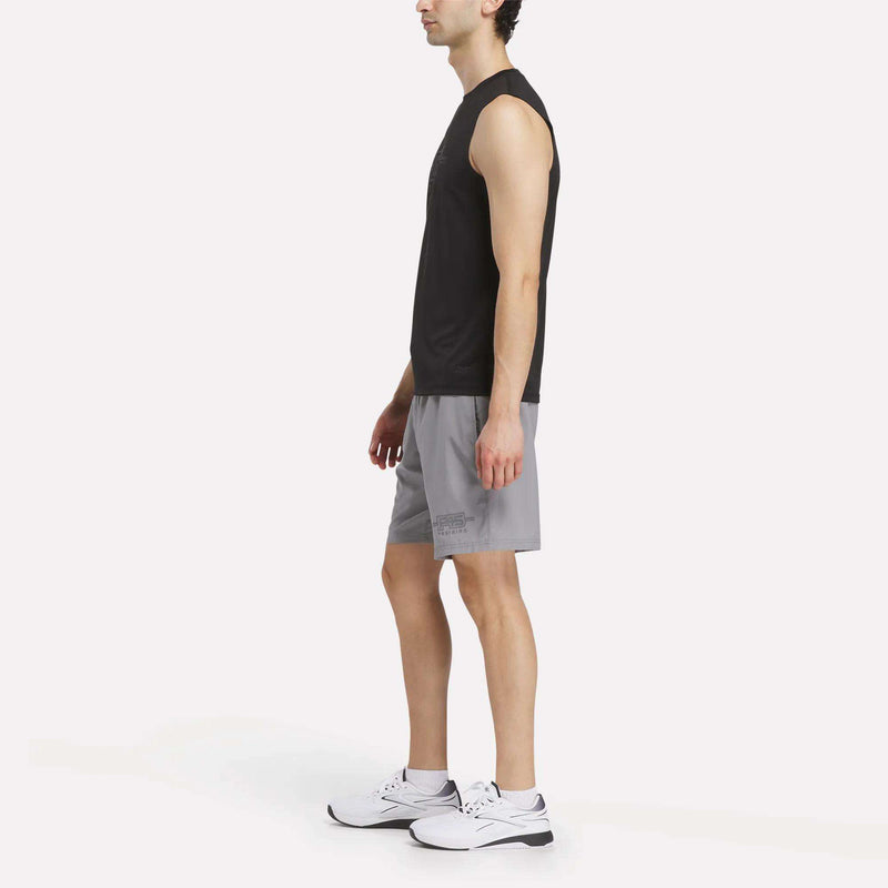 A man in a sleeveless black shirt, Reebok Men's Reebok x F45 Training Woven Shorts, and white sneakers stands in profile against a plain white background, ready for high-intensity training.
