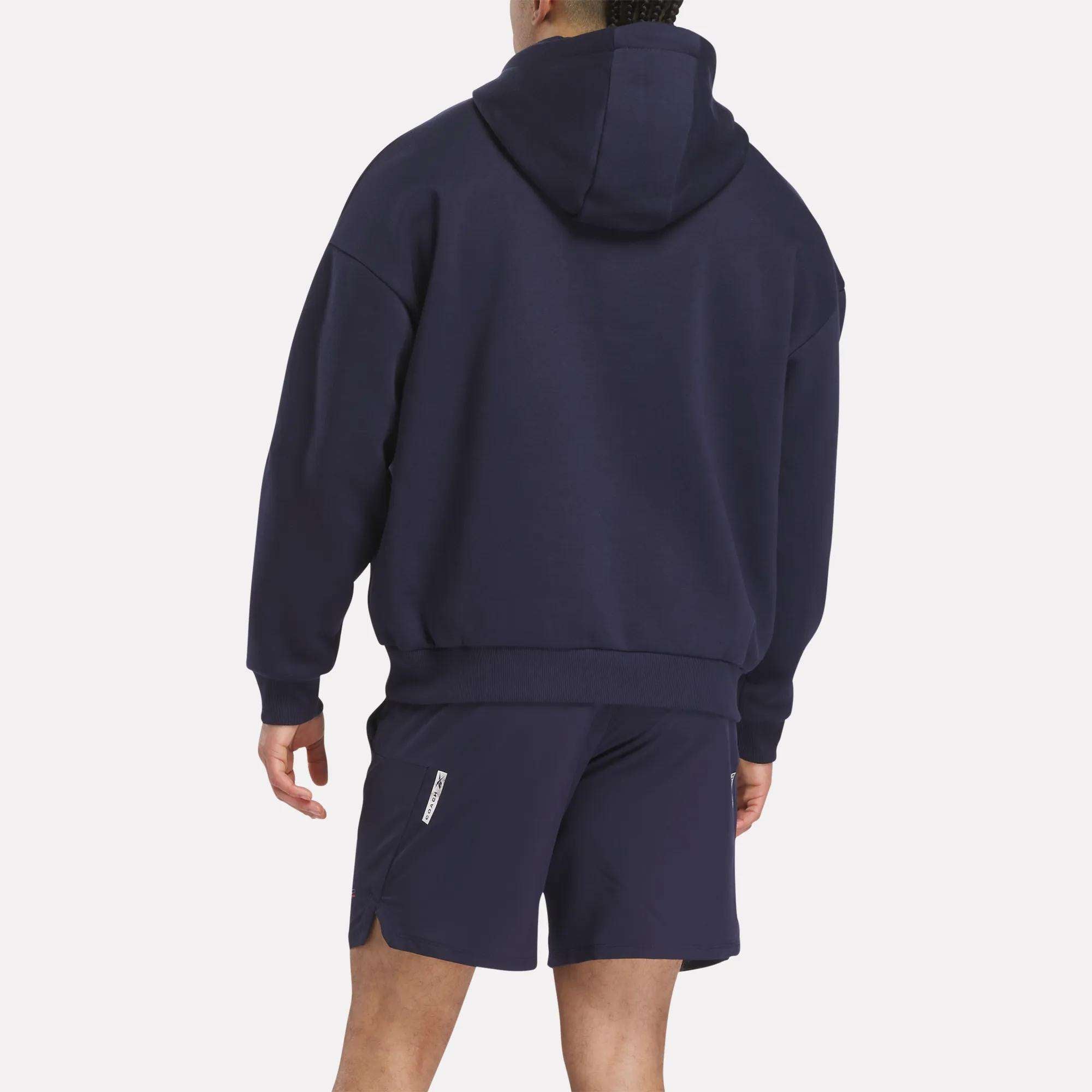 A person faces away from the camera, wearing a dark blue Men's Reebok x F45 Training Coach Fleece Hoodie. The background is plain white.