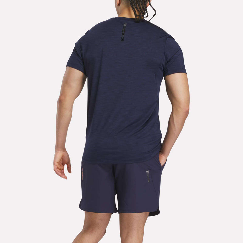 A man with braided hair is seen from the back, wearing a navy Men's Reebok x F45 Training Coach T-Shirt and matching shorts with zippered pockets, standing against a plain white background.