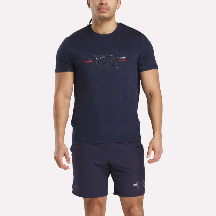 A man stands facing forward against a white background, wearing a navy blue Reebok x F45 Training Coach T-Shirt with a small chest graphic, paired with matching navy blue shorts.