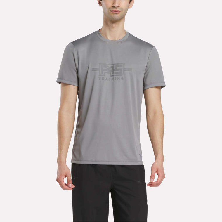 A man wears the Reebok Men's Reebok x F45 Training T-Shirt in Grey 3, featuring performance design and "RS TRAINING" print on the front, paired with black pants and standing against a plain white background.