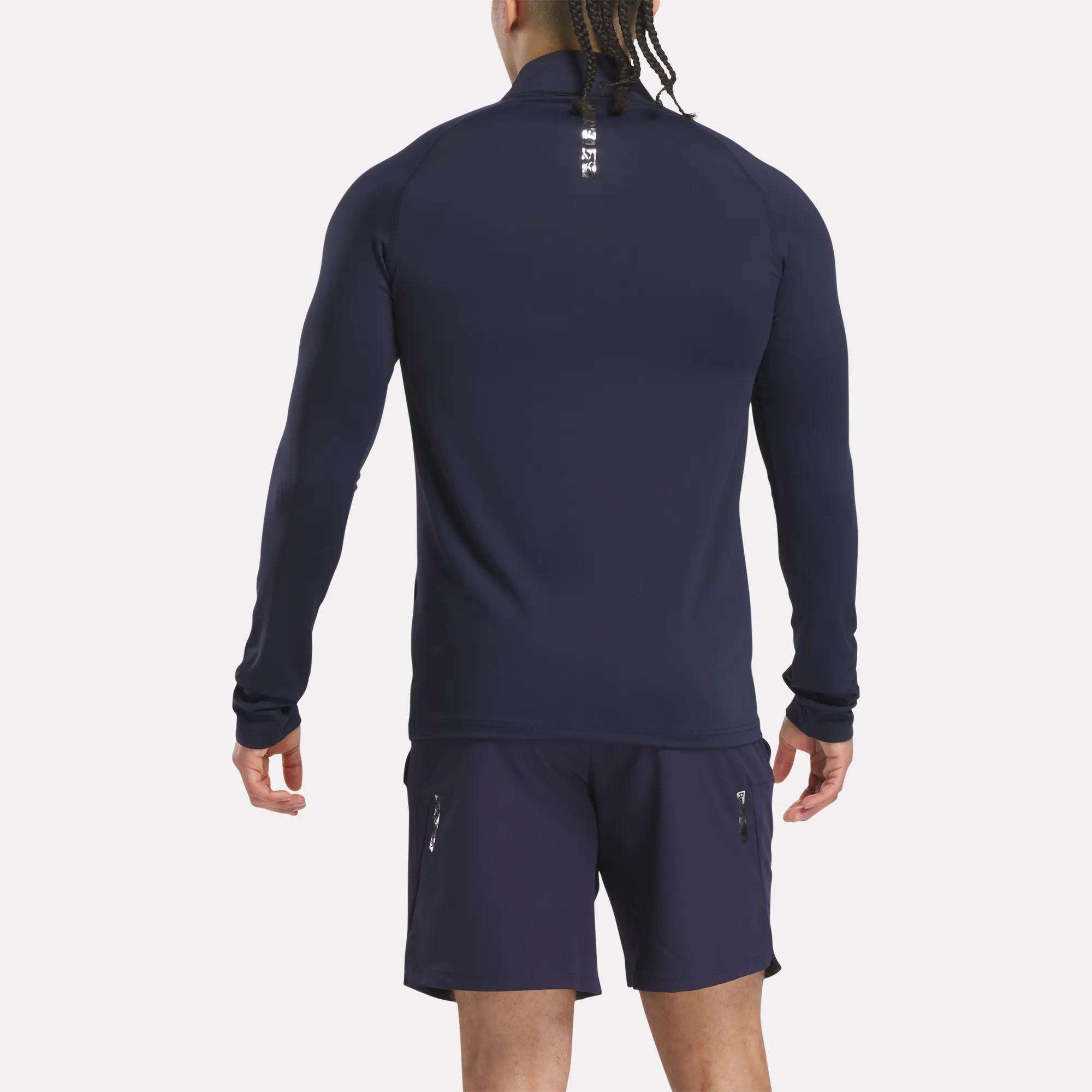 A man with braided hair stands with his back to the camera, wearing a Reebok Men's Reebok x F45 Training Coach Quarter-Zip Top in navy against a plain white background.