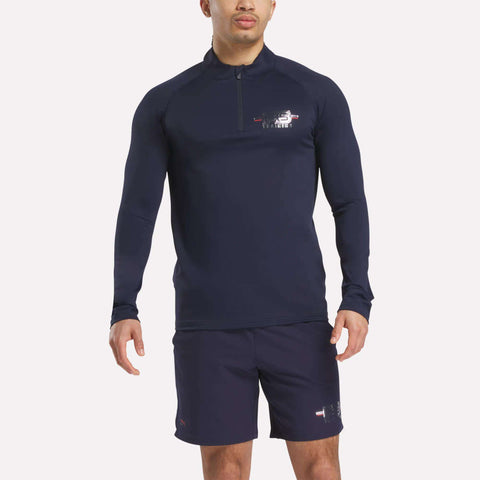 A man wears a navy Men's Reebok x F45 Training Coach Quarter-Zip Top with matching shorts, standing against a plain white background.