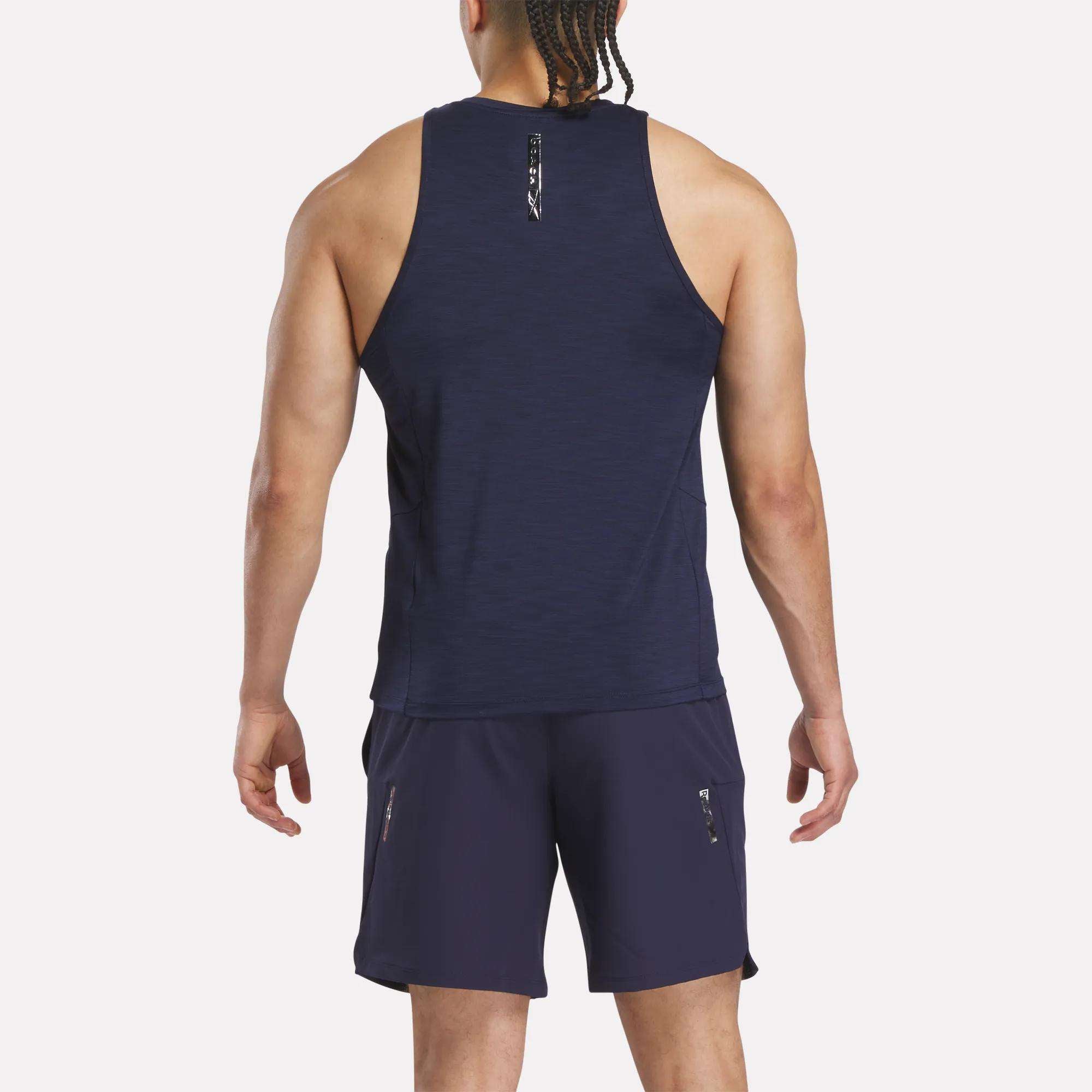 A man with braided hair is seen from behind, wearing a navy blue Reebok x F45 Training Coach Tank Top and matching shorts with zippered pockets, standing against a plain white background.