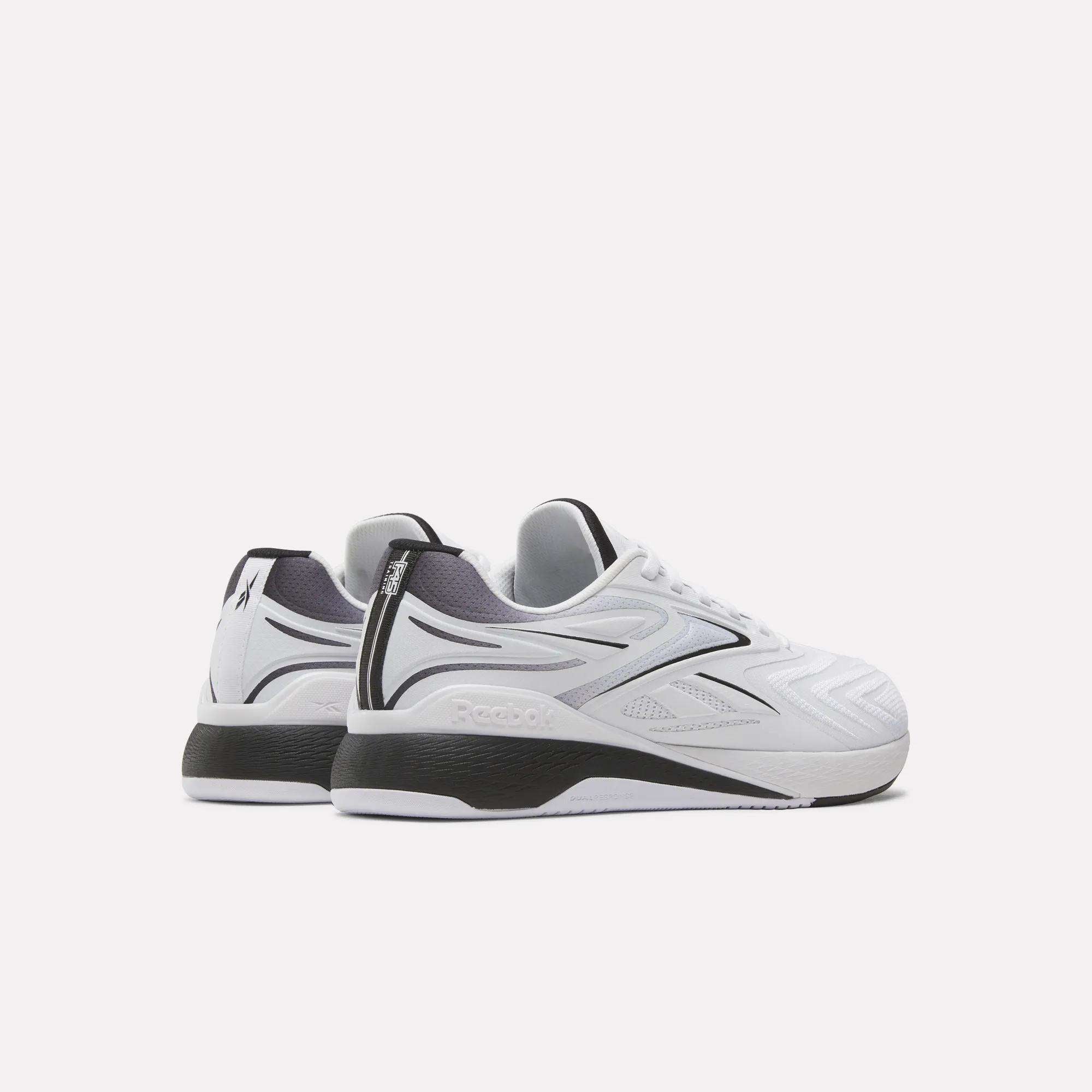 A pair of Reebok x F45 Nano X5 Edge training shoes in white with black accents is displayed from the back and side on a light background. These Reebok sneakers feature textured details and a thick sole, making them ideal workout shoes.