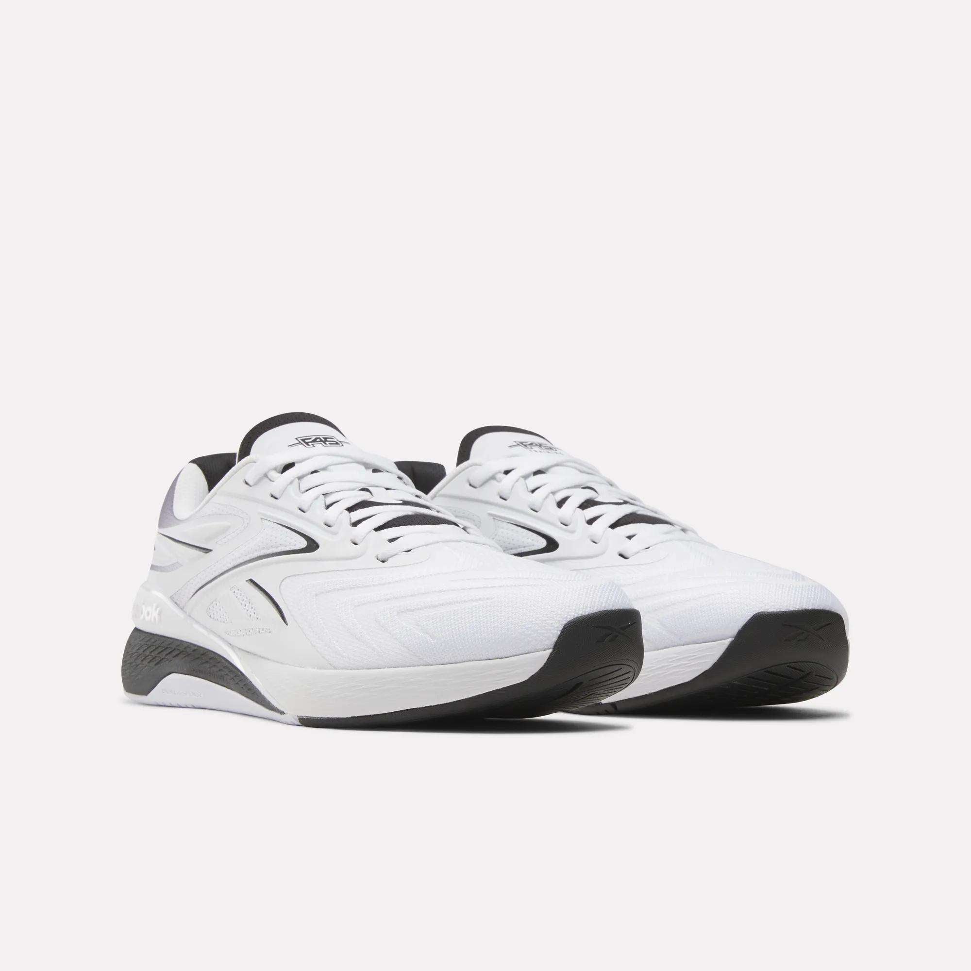 A pair of Reebok x F45 Nano X5 Edge sneakers by Reebok, white with black soles and accents, are displayed side by side at an angle on a plain light background.