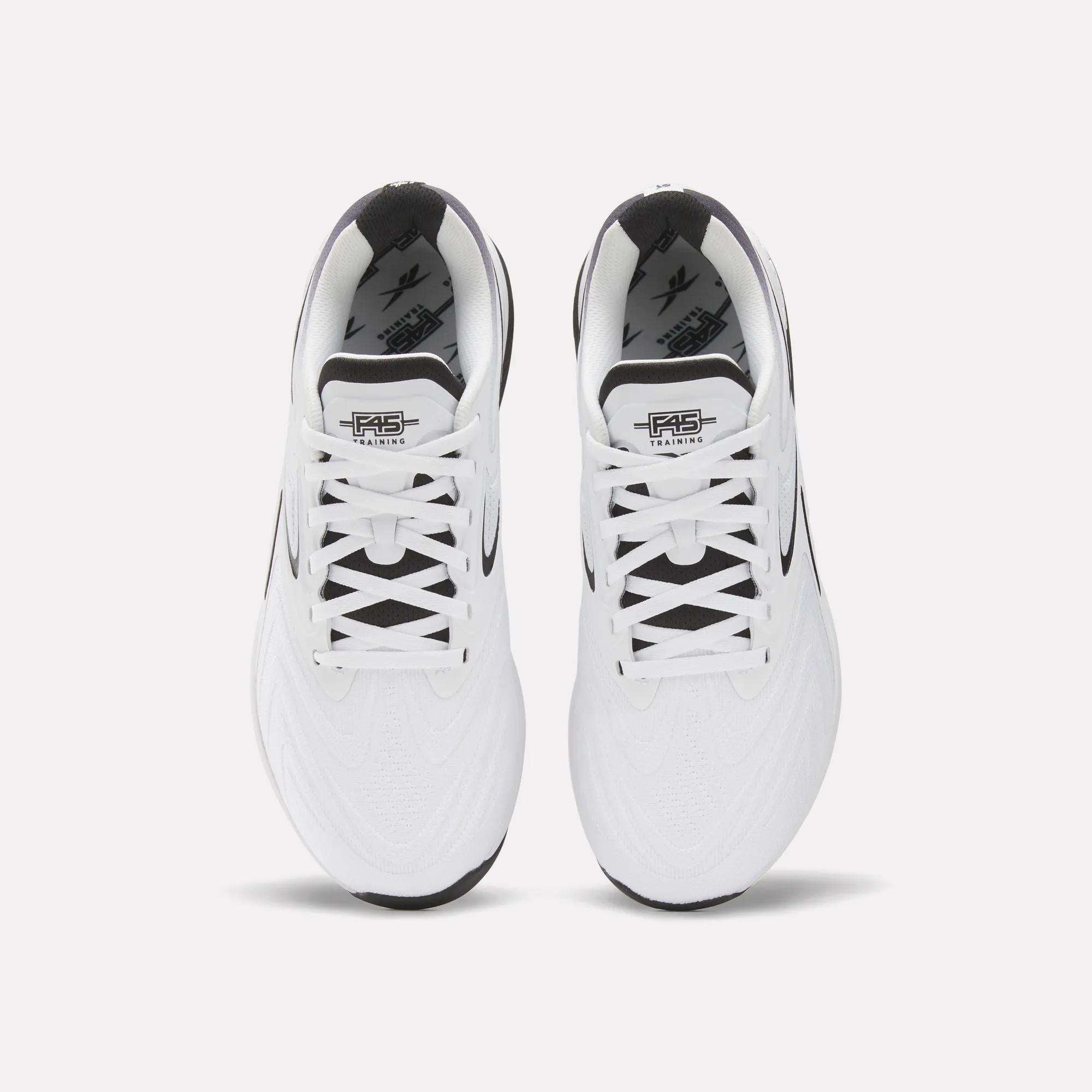 Top view of a pair of white Reebok x F45 Nano X5 Edge training shoes with black accents and white laces, featuring the F45 Training logo on the tongue, placed side by side on a plain background.