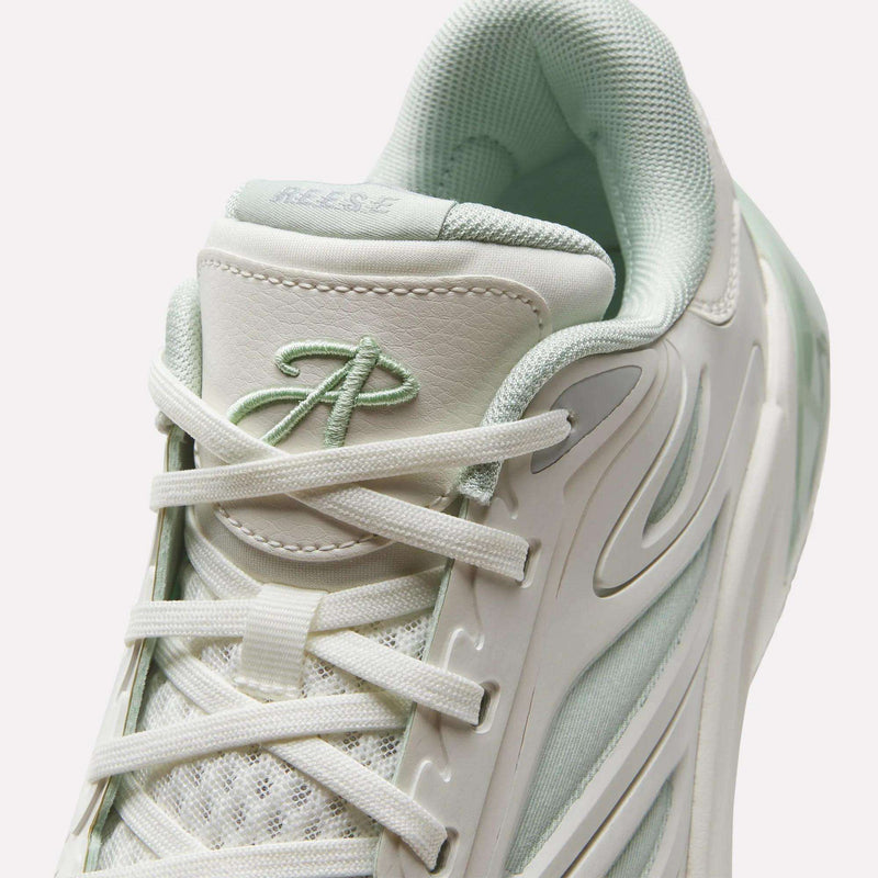 A close-up of the Angel Reese 1 Basketball Shoes by Reebok in white and light green, highlighting the laces, mesh upper, and a stitched ‘A’ logo on the tongue—these performance basketball sneakers feature Reebok’s Energy Return System for enhanced support on the court.
